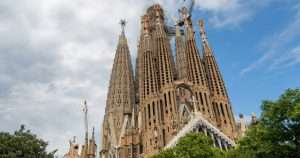 Sagrada Família in Barcelona with tall spires, ornate stonework, and cranes against a partly cloudy sky.
