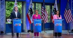 Three speakers stand behind blue lecterns labeled 'Decision 2026' at a political event, with California and U.S. flags in the background.
