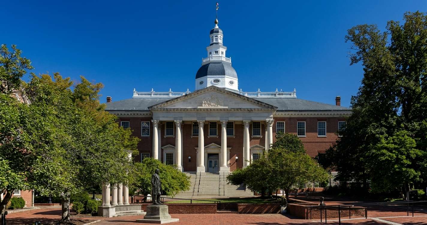 Brick university building with a white-columned portico, dome, and statue in a tree-lined plaza.