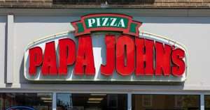 Papa John's pizza sign on a storefront, with bold red letters spelling PAPA JOHN'S and a green banner reading PIZZA.